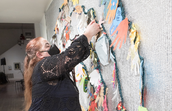 Artist Maia Scott places additional paper hands to her sculpture, 'One Peace Labyrinth', a colorful participatory tapestry of fabric weaving paper hands in a labyrinth pattern.